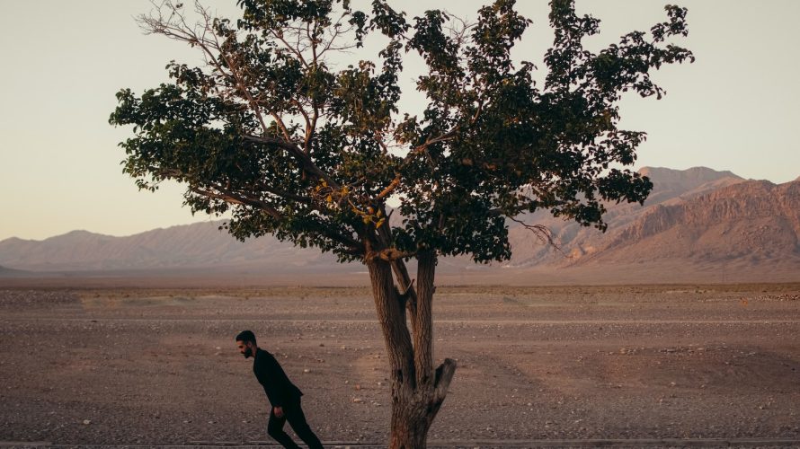 a man walking past a tree in the middle of a desert